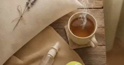 Flat lay : tisane camomille, spray nasal eau de mer, balle de tennis et lavande sur drap beige pour l'apnée du sommeil