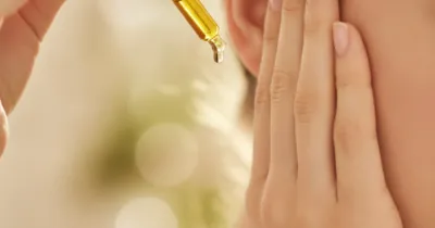 Gros plan sur une main tenant un compte-gouttes d'huile d'olive près de l'oreille pour déboucher un bouchon de cérumen naturellement