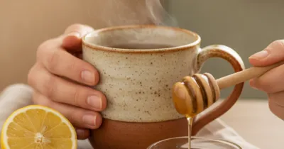 Mains tenant une tasse fumante de grog au miel et citron avec du gingembre frais