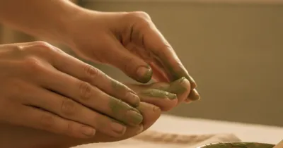 Mains massant un pied avec de l'argile verte pour soulager un hallux valgus