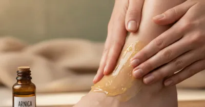 Mains massant délicatement une cheville gonflée avec du gel d'arnica, flacon d'arnica et feuilles de sauge à proximité