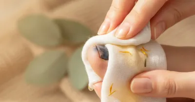 Gros plan sur des mains de femme appliquant délicatement une compresse froide d'arnica sur un ongle bleu noir