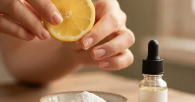 Gros plan des mains de femme frottant délicatement un citron sur un ongle jauni, bicarbonate et huile d'arbre à thé à côté, lumière naturelle douce