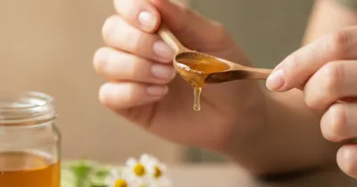 Gros plan sur des mains appliquant du miel sur les coins des lèvres avec une cuillère en bois, remèdes naturels contre la perlèche